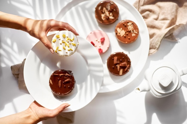 Las manos de las mujeres corregirán los minipies con chocolate con leche de frambuesas de coco Una variedad de postres deliciosos y coloridos sobre un fondo brillante con sombras Comida dulce