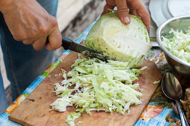 Las manos de las mujeres cortan el repollo en la mesa.