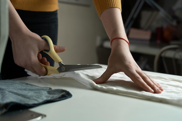 Las manos de las mujeres cortan tela en un patrón de papel con tijeras de sastre en una mesa blanca Una modista en el trabajo en un estudio de costura Espacio de copia