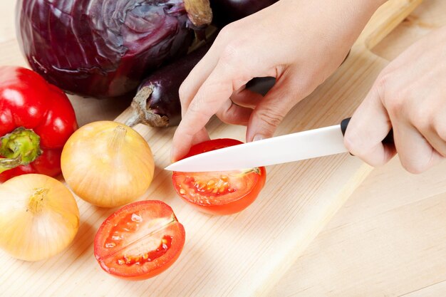 Las manos de las mujeres con un cuchillo cortan verduras en una tabla de cortar