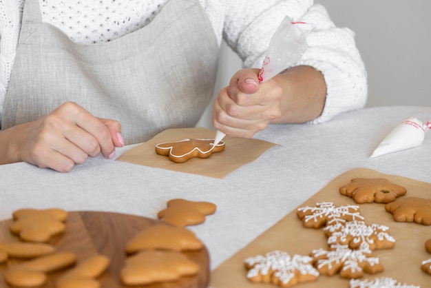 Las manos de las mujeres decoran el azúcar glaseado casero tradicional galletas de Año Nuevo copo de nieve hombre de pan de jengibre