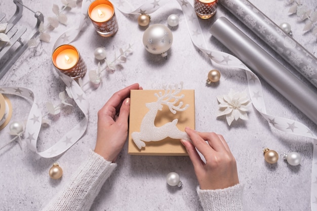 Las manos de las mujeres decoran la caja de regalo de Navidad con adornos blancos Concepto de vacaciones de invierno