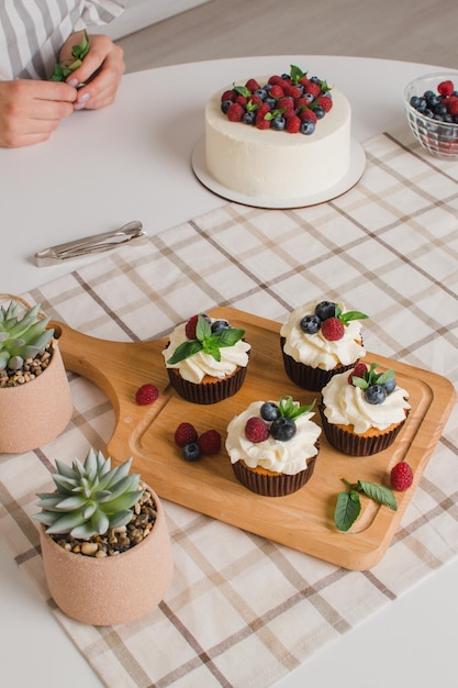 Las manos de las mujeres decoran muffins con arándanos frescos, frambuesas y hojas de menta. inglés