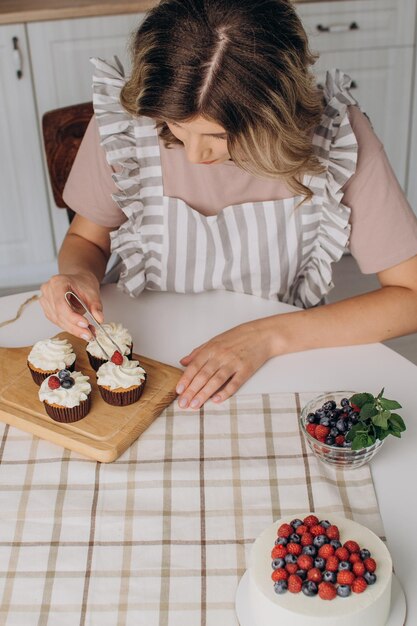 Las manos de las mujeres decoran muffins con arándanos frescos, frambuesas y hojas de menta.