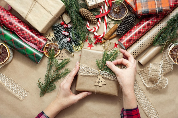 Las manos de las mujeres empacan y decoran un regalo de Navidad, la mesa está cubierta con papel artesanal beige y