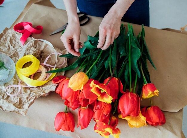 Las manos de las mujeres empacan un ramo festivo en papel de regalo La floristería hace una asamblea con tulipanes rojos en el taller Una mujer en el trabajo pequeña empresa o pasatiempo