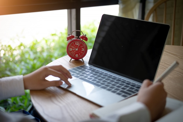 Manos de mujeres escribiendo en el teclado de la computadora y escribiendo una nota, horario de negocios y fecha límite