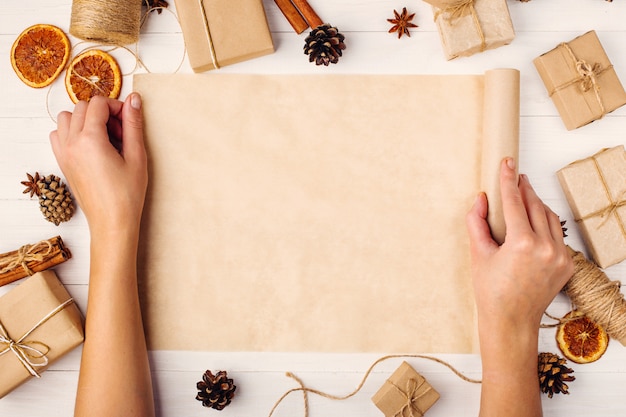 Las manos de las mujeres están girando el rollo de papel artesanal Contra el fondo de la mesa de madera. , vista superior, lugar para el texto.