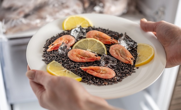 Las manos de las mujeres están sacando un plato de arroz negro, camarones y limón del congelador de la nevera.