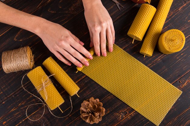 Las manos de las mujeres hacen velas artesanales de cera natural con textura de panal de abejas, sobre una mesa de madera.