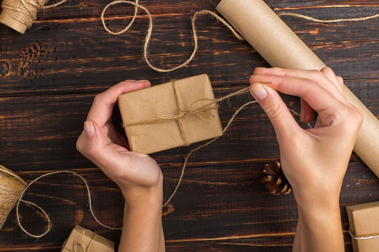 Foto manos de mujeres haciendo un regalo de papel artesanal.