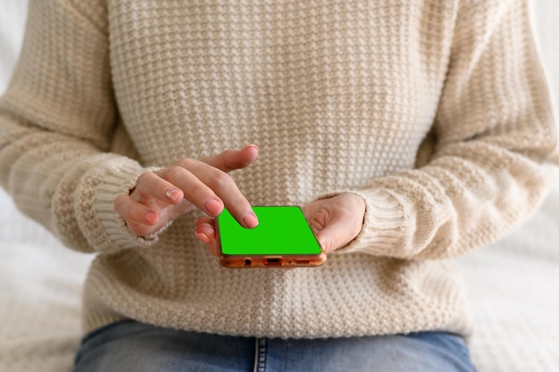 Las manos de las mujeres en un jumper blanco sostienen un teléfono inteligente en sus manos Celular