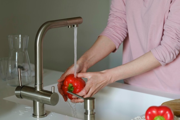 Las manos de las mujeres lavan el pimiento rojo con agua corriente en el fregadero Estilo de vida saludable