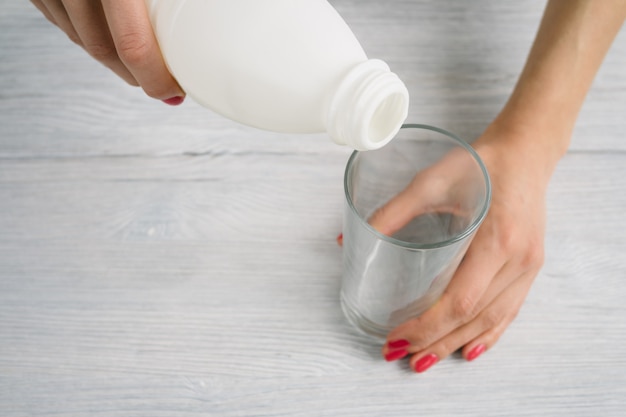 Las manos de las mujeres con una manicura roja vierten el yogur en una taza de vidrio vacía