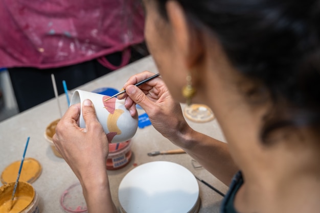 Manos de mujeres pintando un objeto de cerámica