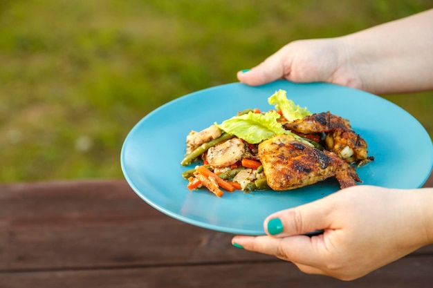 Las manos de las mujeres ponen un plato con pollo y verduras sobre la mesa.