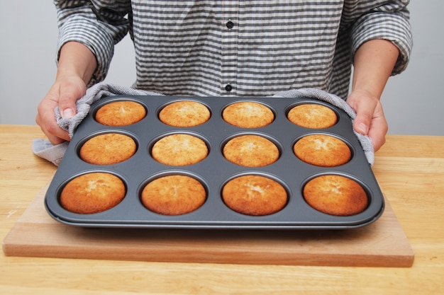 Foto las manos de las mujeres que sostienen el molde de metal con muffins.