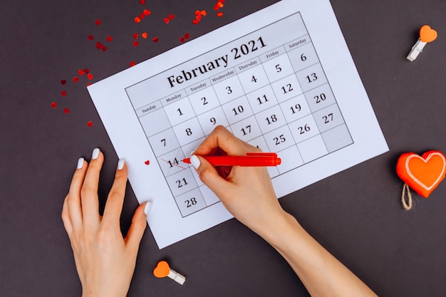 Las manos de las mujeres rodearon el número 14 del calendario con lápiz labial rojo. Día de San Valentín.