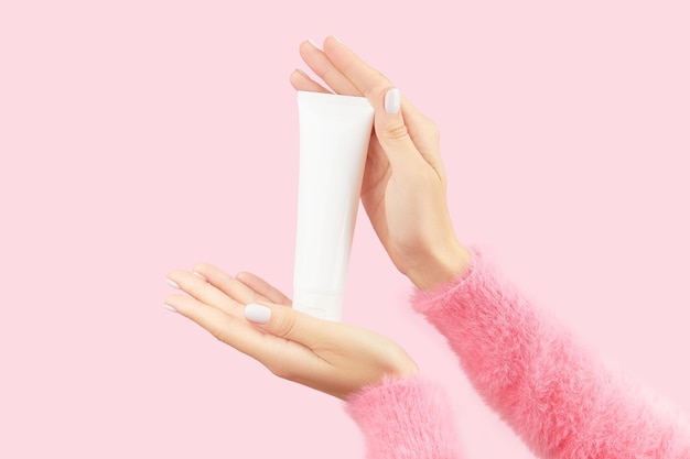 Las manos de las mujeres sosteniendo un tubo blanco sobre un fondo rosa pastel concepto de tratamiento de belleza de cuidado personal