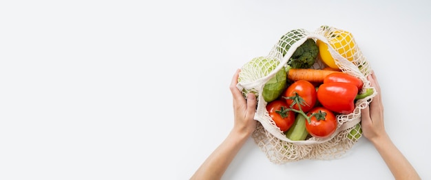 Las manos de las mujeres sostienen una bolsa con verduras frescas en una mesa blanca Vista superior plana Lay Banner