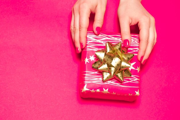 Las manos de las mujeres sostienen una caja de regalo sobre un fondo rosa