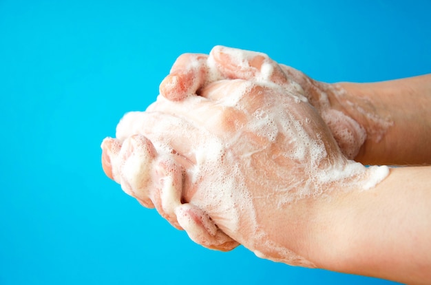 Las manos de las mujeres sostienen jabón. Espuma de jabón en las manos. Jabón amarillo en las manos. La mujer lava el jabón con vista lateral de las manos sobre un fondo azul. Protección contra el virus. COVID-19