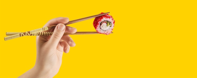 Las manos de las mujeres sostienen rollos de sushi con palos. Fondo amarillo. Concepto creativo