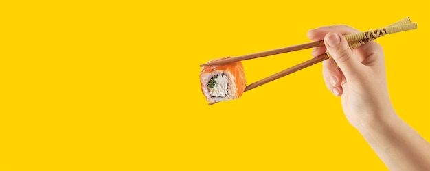 Las manos de las mujeres sostienen rollos de sushi con palos. Fondo amarillo. Concepto creativo