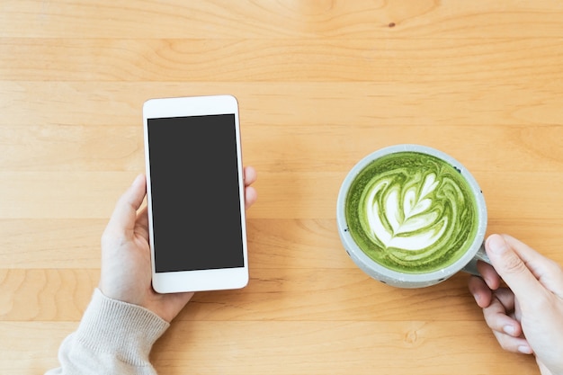 Las manos de las mujeres sostienen una taza de té verde con leche mientras usan la tecnología del teléfono, bebidas, concepto de estilo de vida