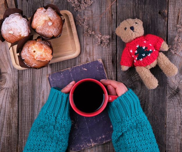 Foto las manos de las mujeres en un suéter de punto verde que sostiene una taza de cerámica roja con café negro