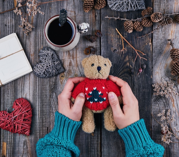 Las manos de las mujeres en un suéter verde sostienen un viejo oso de peluche marrón.