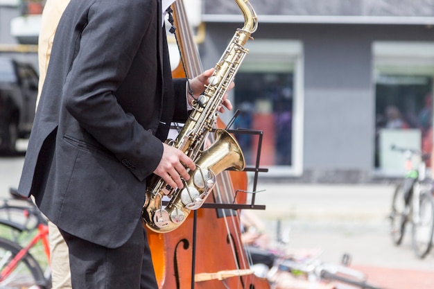 Manos de músico callejero tocando saxofón y contrabajo en un entorno urbano