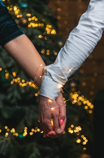 Manos de Navidad de hombre y mujer en guirnaldas juntos. Enfoque selectivo. fiesta.