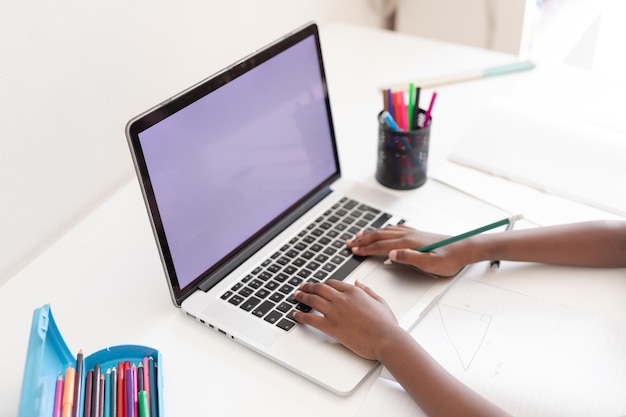 Manos de niña afroamericana en el escritorio usando una computadora portátil con espacio de copia para la lección de la escuela en línea