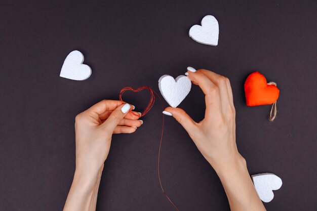 Las manos de la niña decoran un corazón blanco como regalo a su amado, para el día de todos los enamorados. Dia de San Valentin. Hay muchos corazones blancos en el círculo.