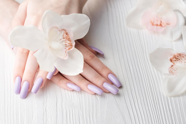 Manos de niña con delicadas flores de orquídeas y manicura púrpura