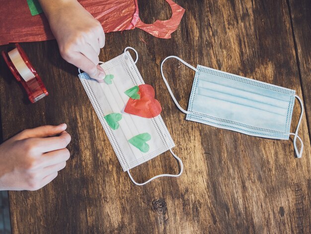 Manos de una niña haciendo manualidades con papel y decorando una mascarilla quirúrgica