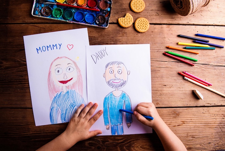 Foto manos de una niña irreconocible dibujando fotos de su madre y su padre estudio filmado en fondo de madera