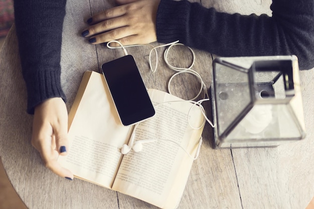 Manos de niña con un libro y un teléfono inteligente con auriculares