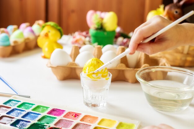 Manos de una niña pintan huevos con pinturas al agua para Pascua.