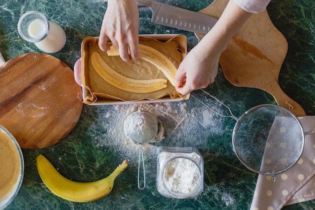 Las manos de la niña ponen el plátano cortado en la masa de pastel.