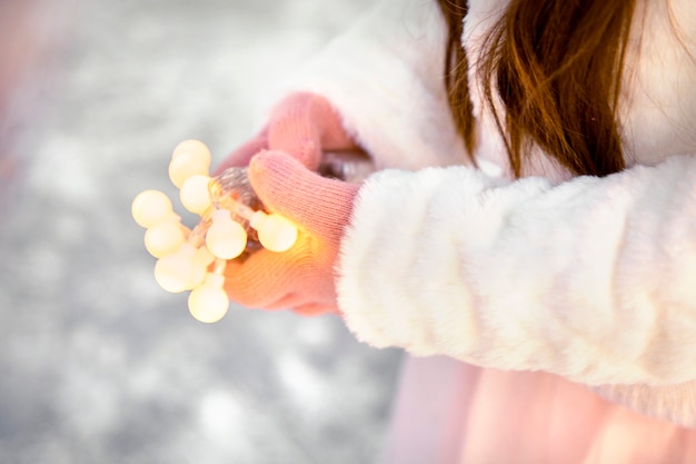 Manos de niña sosteniendo una cadena de luces bokeh