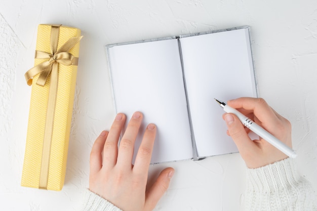 Las manos de la niña sostienen un cuaderno en blanco entre caja de regalo. Metas, planes, sueños, lista de cosas por hacer