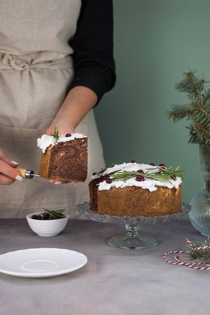 Las manos de la niña sostienen un trozo de pastel de Navidad con bayas rojas sobre una mesa gris