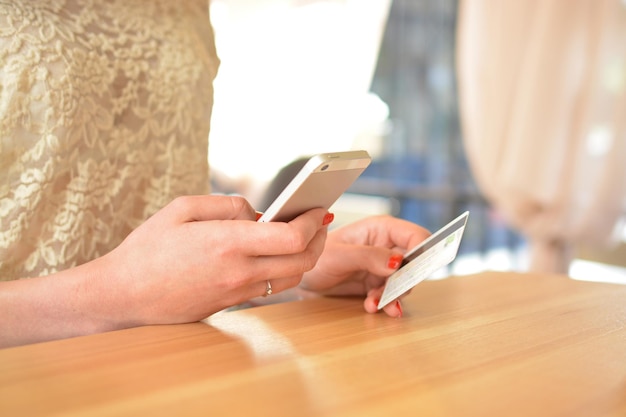 Manos de una niña con un teléfono inteligente móvil y una tarjeta de crédito en una mesa de madera