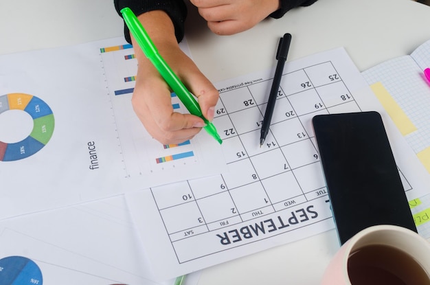 Manos de niña con teléfono móvil con escritura de calendario y lista de trabajo en diario en el escritorio