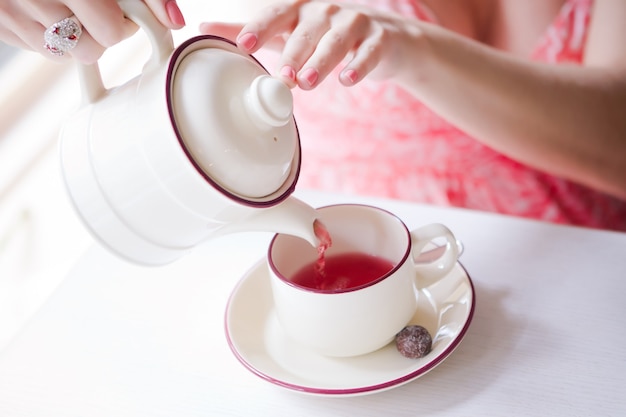 Las manos de una niña vierten té de una tetera en taza blanca