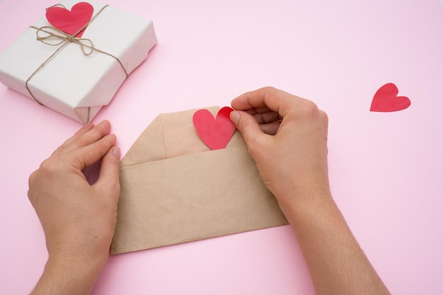 Manos de niñas preparando un regalo para el Día de San Valentín San Valentín hecho a mano y un sobre en un rosa