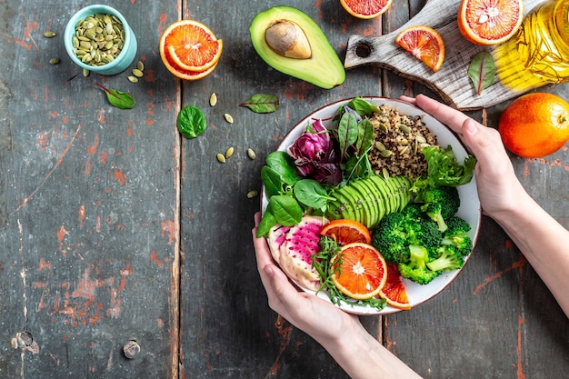 Manos de las niñas sosteniendo el cuenco de Buda vegetariano vegetal de quinua con frutas, verduras y semillas. vista superior.