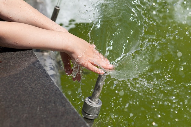 Las manos del niño se bañan en una fuente en el parque de la ciudad Splash International Childrens Day